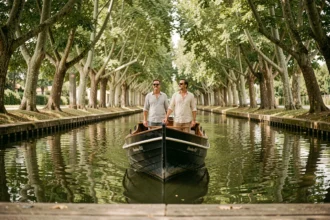Péniche traditionnelle naviguant sur le Canal du Midi sous un tunnel d'arbres, couple à bord profitant de la croisière en pension complète